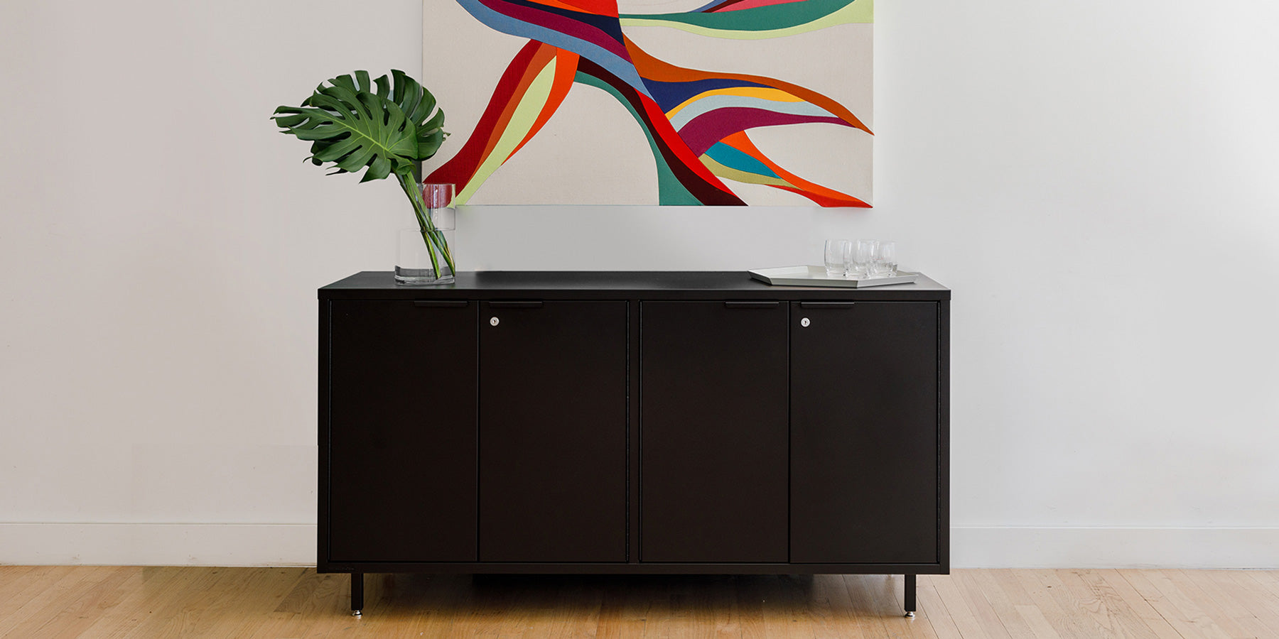 Heartwork Active Duty storage credenza in black against white wall with a painting in the background