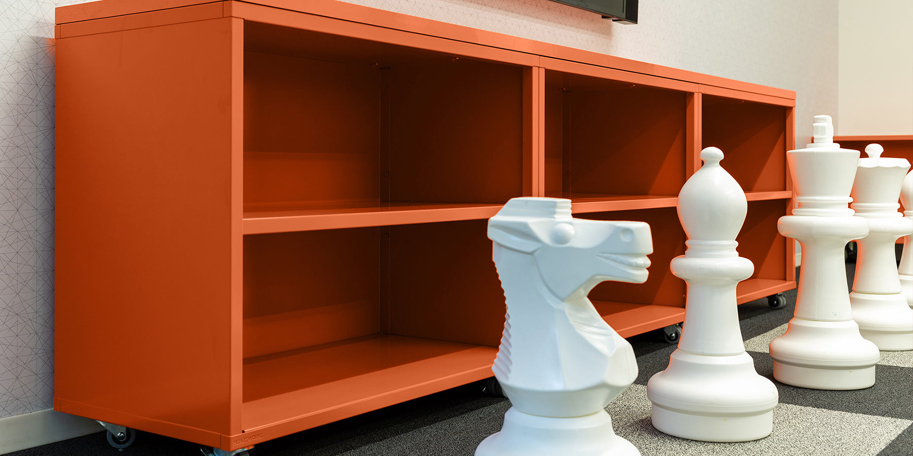 Heartwork Building Block bookcase in warm orange staged with giant white chess pieces